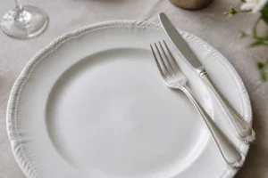 Assiette blanche sur nappe en lin avec fourchette et couteau en position 16h20 pour signifier la fin du repas