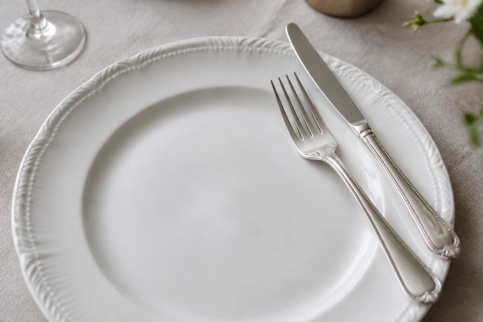 Assiette blanche sur nappe en lin avec fourchette et couteau en position 16h20 pour signifier la fin du repas
