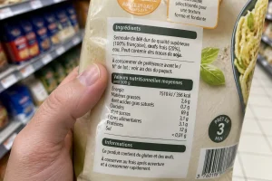 Main tenant un emballage alimentaire avec la liste des ingrédients mentionnant l'additif E471 visible